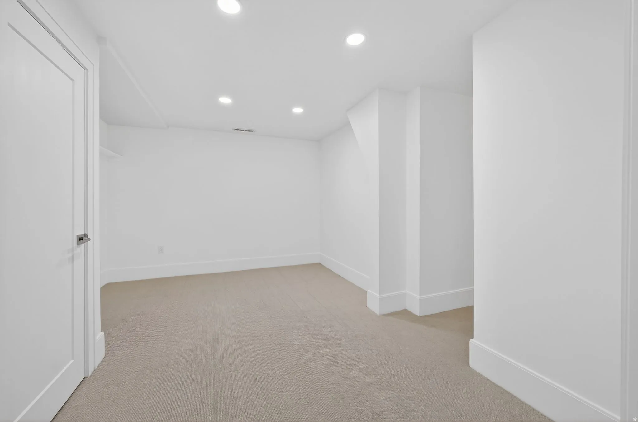 Neutral-toned carpeting spans this spacious room, featuring recessed lighting and bright white walls