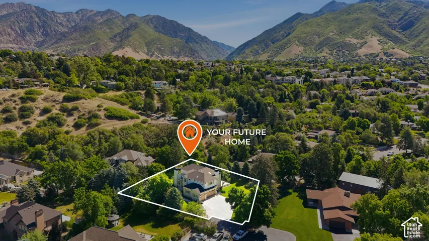 Spacious property featuring a prominent residence, mature trees, and a paved driveway, set against a backdrop of distant mountains and surrounding greenery
