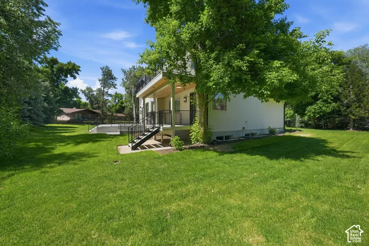 Spacious side lawn area with mature trees and a rear deck featuring black metal railings and stairs