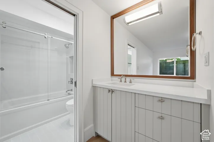 Downstairs bathroom featuring a white vanity with a light-toned countertop, a wood-framed mirror, and a tub with a sliding glass enclosure