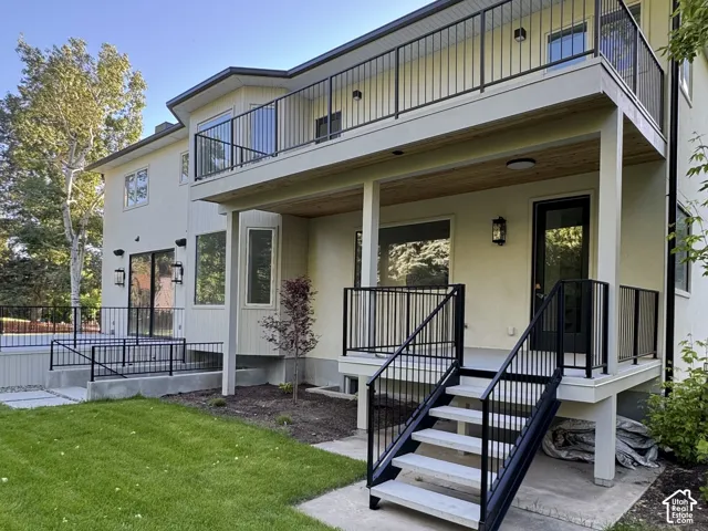 Separate entrance to butler pantry featuring an upper-level balcony to primary suite with glass and metal railings, a ground-level patio, a covered lower-level deck with recessed lighting, and a metal staircase with composite treads