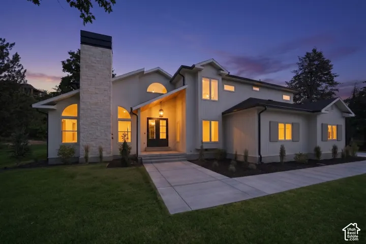 Modern stucco exterior featuring a prominent stone-clad chimney and a dark-framed entry door with side lites