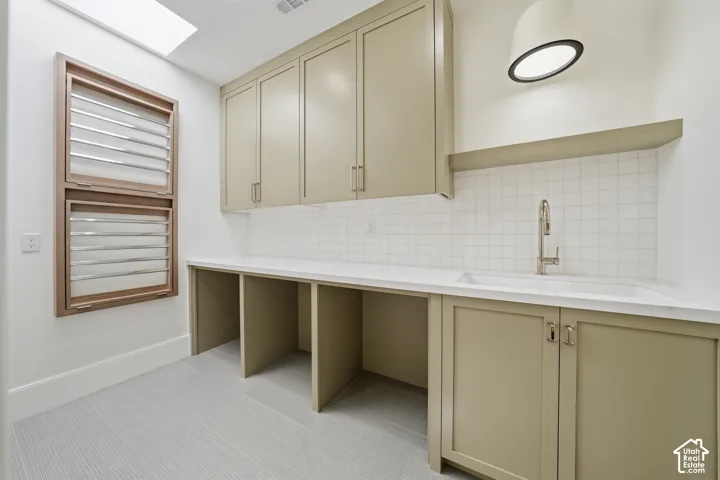Upstairs laundry area featuring a built-in sink with a modern faucet, white subway tile backsplash, and light-toned cabinetry