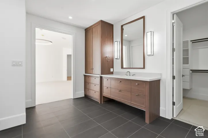 Vanity area featuring dark tile flooring, a wood-finish vanity with ample storage, a countertop, and a framed mirror with two vertical light fixtures