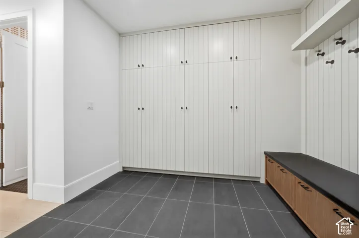 Entryway with built-in storage featuring white paneled cabinetry, dark floor tiling, and a custom wooden bench with integrated storage