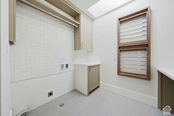 Upstairs laundry area room featuring light-toned cabinetry, a built-in hanging rod, full-height tile backsplash, and a skylight