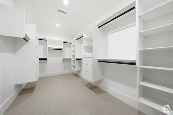 Spacious primary walk-in closet featuring custom white cabinetry, extensive shelving, multiple hanging rods, built-in drawers, and recessed lighting