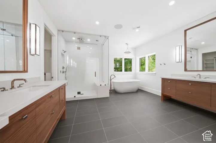 Spacious primary bathroom featuring a freestanding soaking tub, a frameless glass shower enclosure, and dual wood-finish vanities with undermount sinks