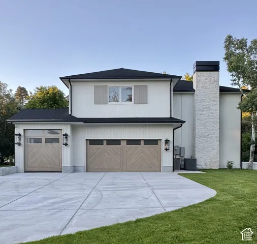 Modern residence featuring a stucco and vertical siding exterior, a prominent stone chimney, and multiple garage doors with chevron paneling
