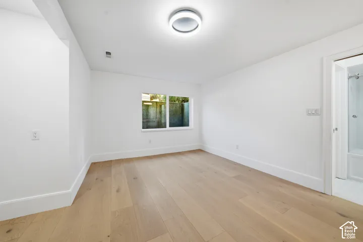 Downstairs room featuring wood-finish flooring, white walls, a single window, and a modern ceiling light fixture