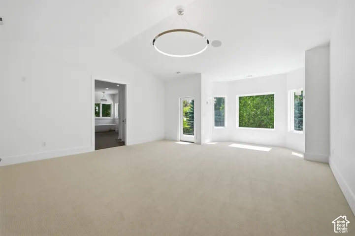 Spacious primary room featuring vaulted ceilings, light-colored carpeting, and a modern circular chandelier