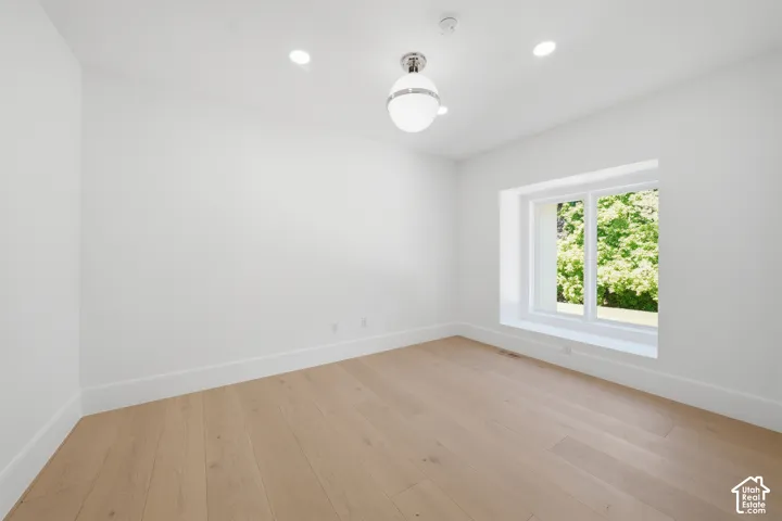 Bright office/ bedroom featuring light wood-finish flooring, white walls, and a recessed window with a deep sill