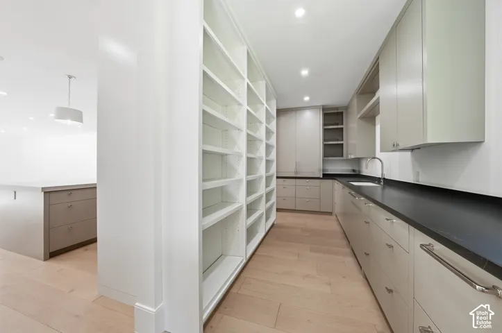Spacious butler pantry kitchen featuring extensive built-in shelving, light wood-finish flooring, recessed lighting, a stainless steel sink, and ample countertop space