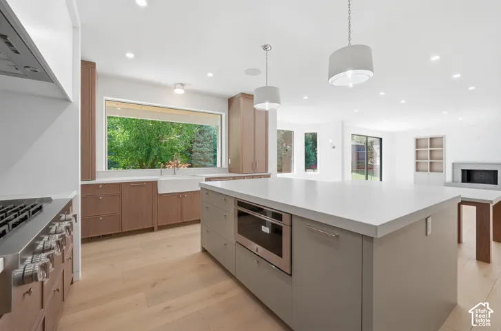 Contemporary kitchen featuring a large center island with integrated microwave, light wood-finish flooring, recessed lighting, and a wide window over the farmhouse sink