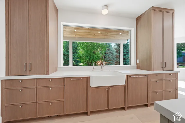 Kitchen featuring expansive full-height cabinetry, a large single-basin farmhouse sink , light wood-finish flooring, and a wide horizontal window with a backyard outlook
