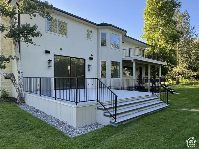 Expansive back patio featuring black metal railings and wide steps to the lawn and overhanging deck off primary suite