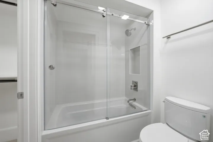 Downstairs modern bathroom featuring a bathtub with a clear sliding glass enclosure, a built-in shower niche, and polished chrome fixtures