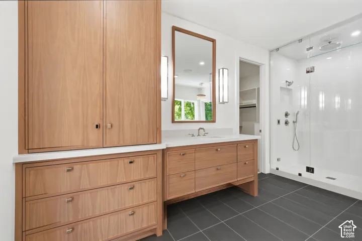 Modern primary bathroom featuring an anti-fog mirrors and glass-enclosed shower with multiple showerheads, a single vanity with a white countertop and wood-finish cabinetry, and built-in wood-finish storage