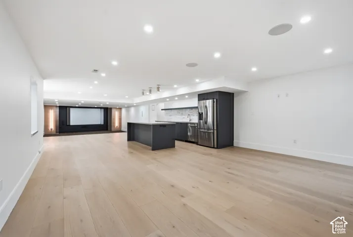 Open-concept recreation area featuring light wood-finish flooring, recessed lighting, and an integrated entertainment screen
