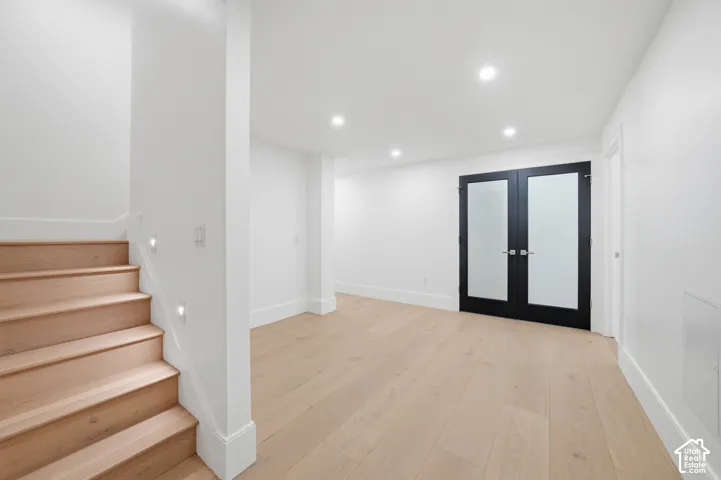 Spacious downstairs room featuring light wood-finish flooring, recessed lighting, and a modern staircase with integrated step lighting