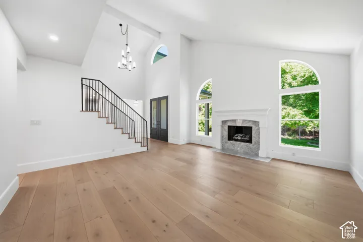 Spacious living area featuring high vaulted ceilings, light wood-finish flooring, and a marble-surround fireplace with a white mantel