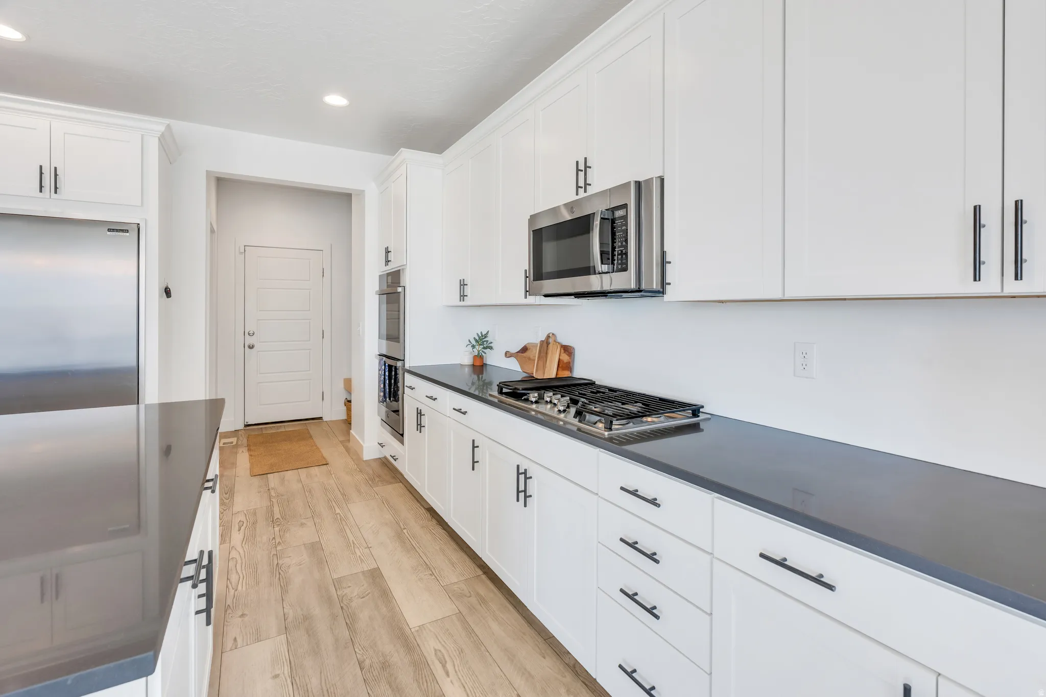 Modern kitchen featuring light wood-finish flooring, white shaker-style cabinetry with matte black hardware, dark countertops, a stainless steel gas range, and a built-in stainless steel microwave