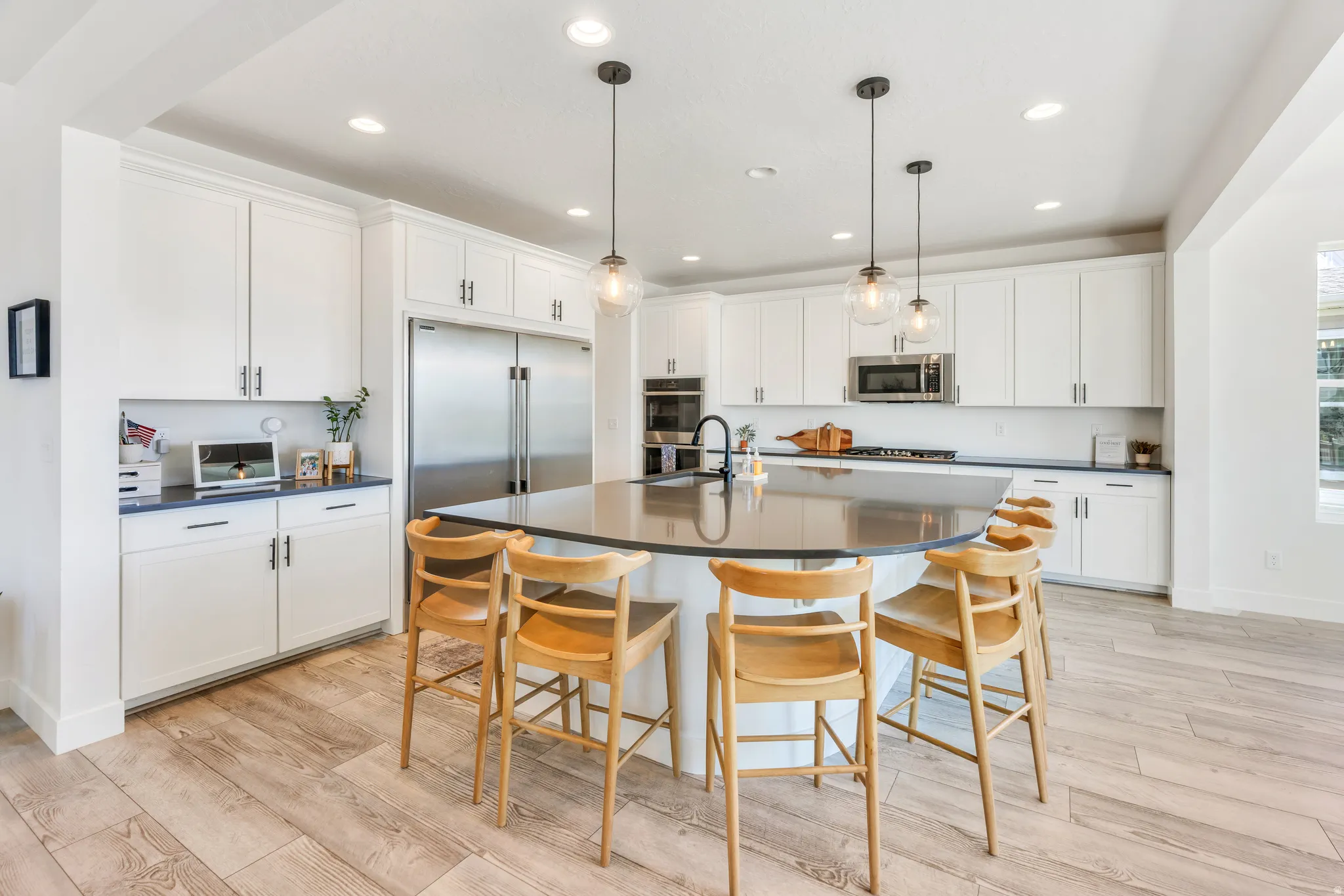 Modern kitchen featuring a large central island with seating, white shaker cabinetry, stainless steel appliances, and wood-finish flooring