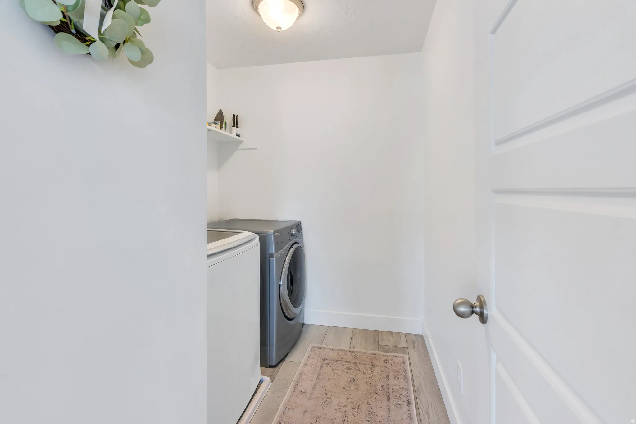 Dedicated laundry area featuring light wood-finish flooring, a white floating shelf, and a ceiling-mounted light fixture