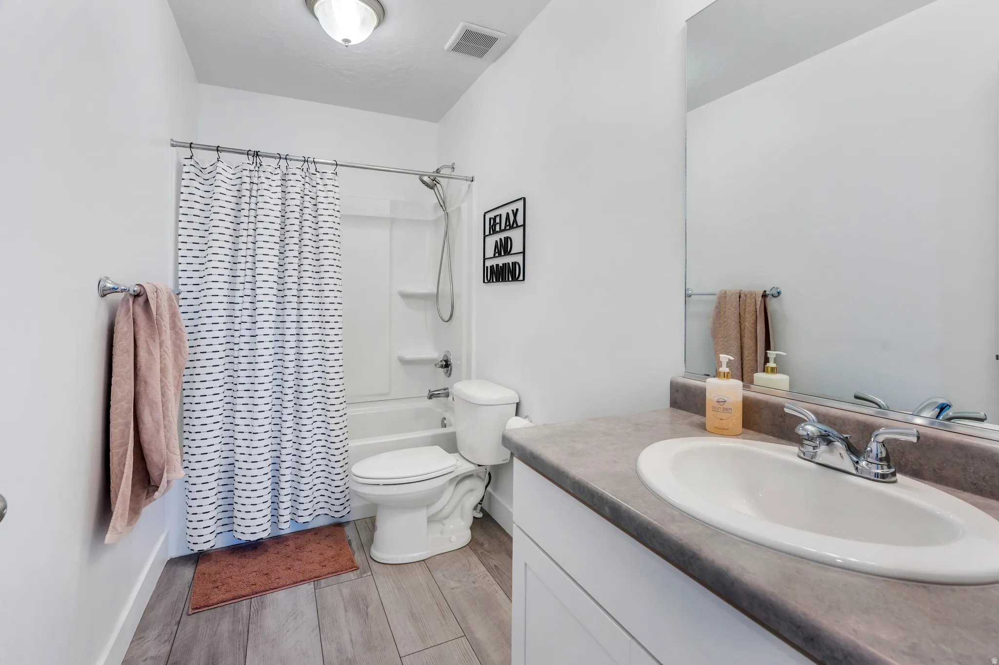 Full bathroom featuring a white tub/shower combination, wood-finish flooring, a vanity with an integrated sink, and a large wall-mounted mirror