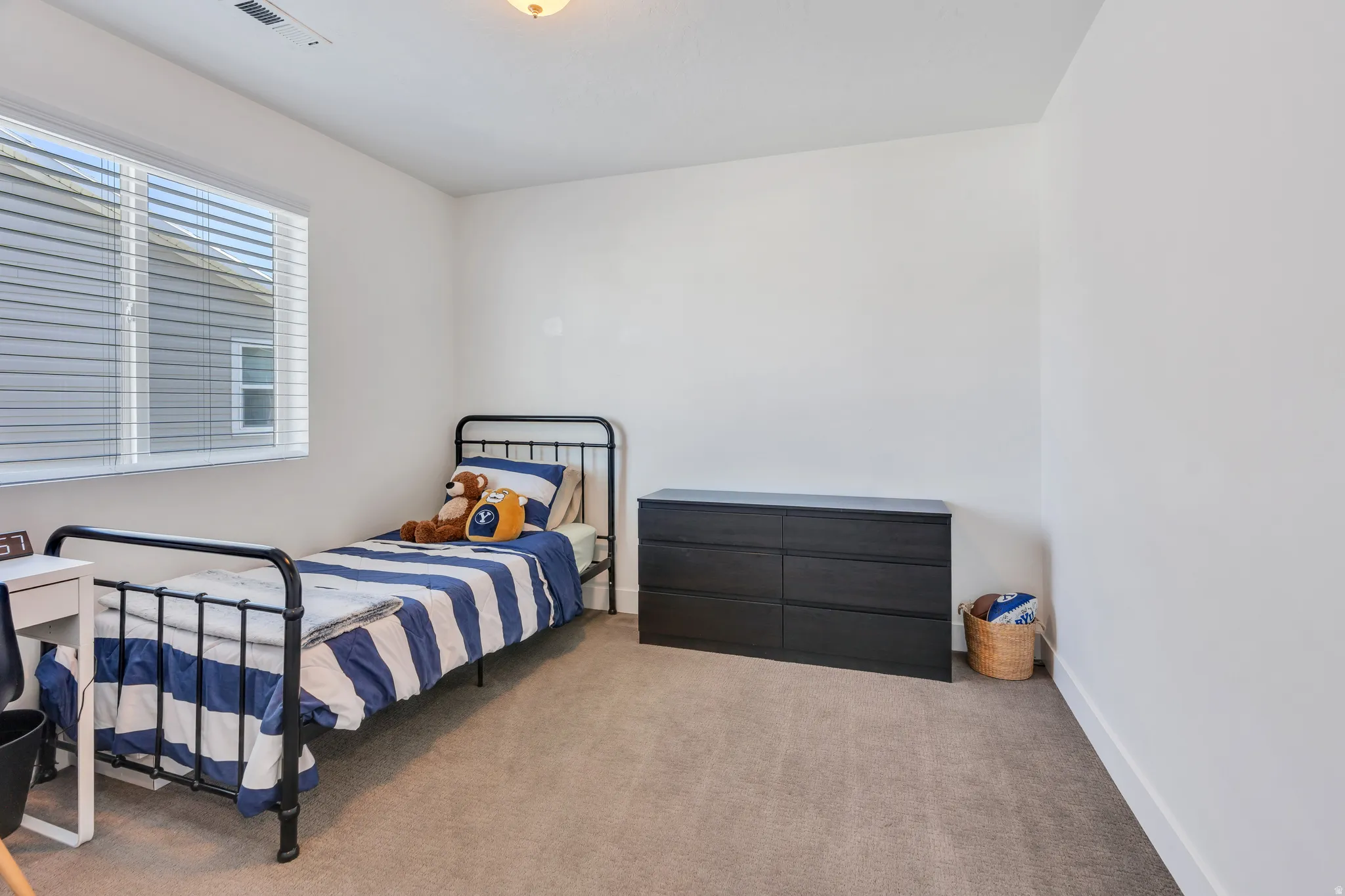 Bright room featuring light gray carpeting, neutral white walls, and a large window with horizontal blinds