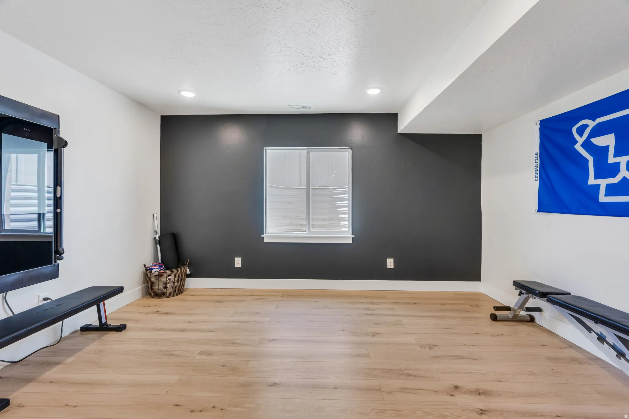 Spacious room featuring light wood-finish flooring, recessed lighting, and a window with white louvered shutters