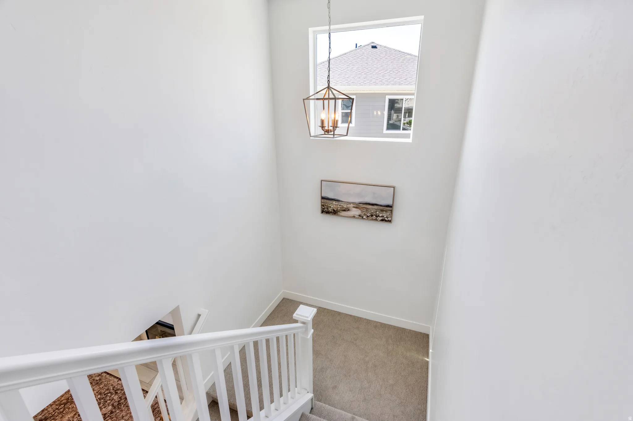 Open stairway featuring white painted banisters, a large upper-level window, and a decorative pendant light fixture