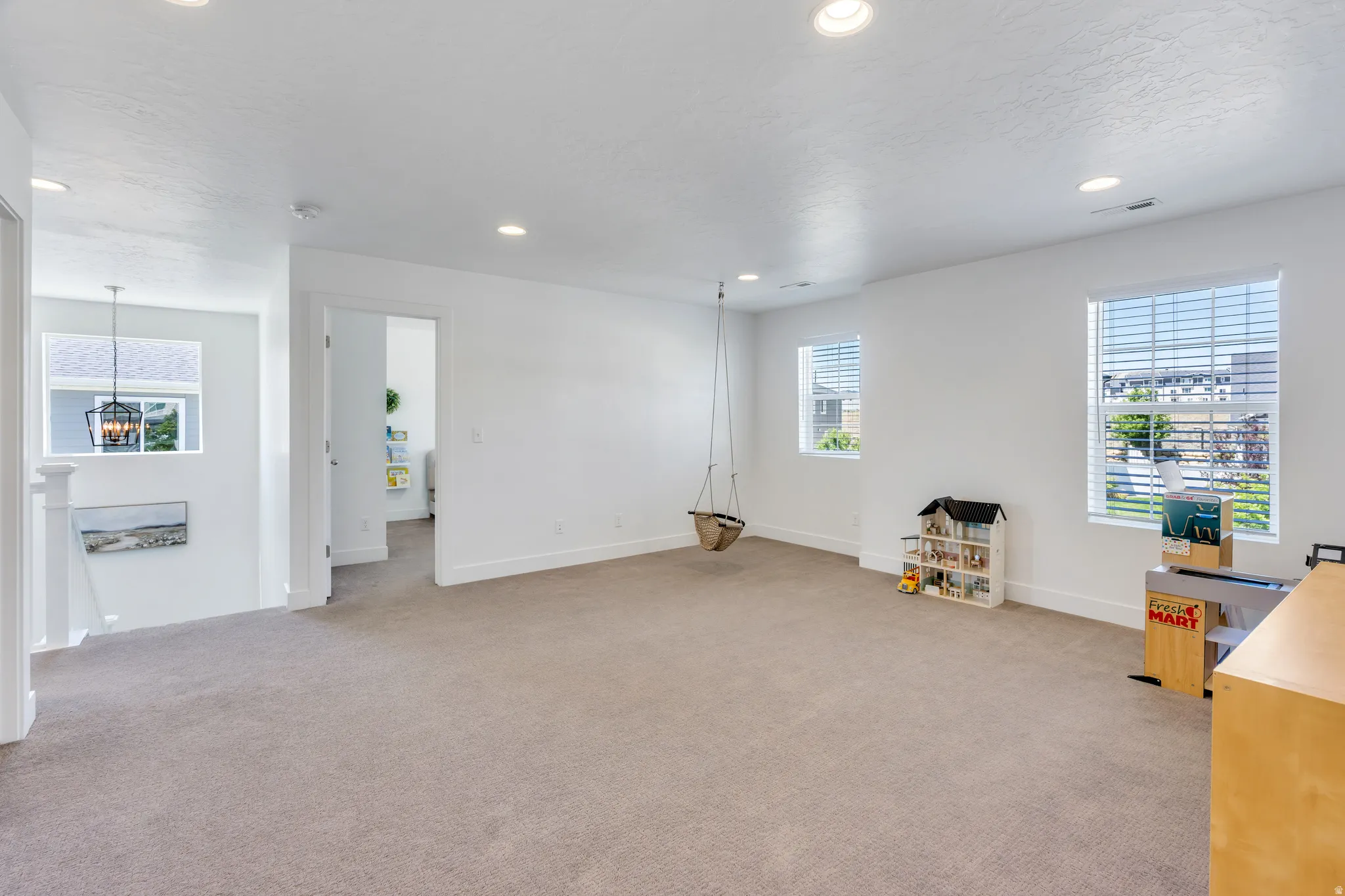 Spacious carpeted room featuring white walls, multiple windows with blinds, recessed lighting, and a broad doorway