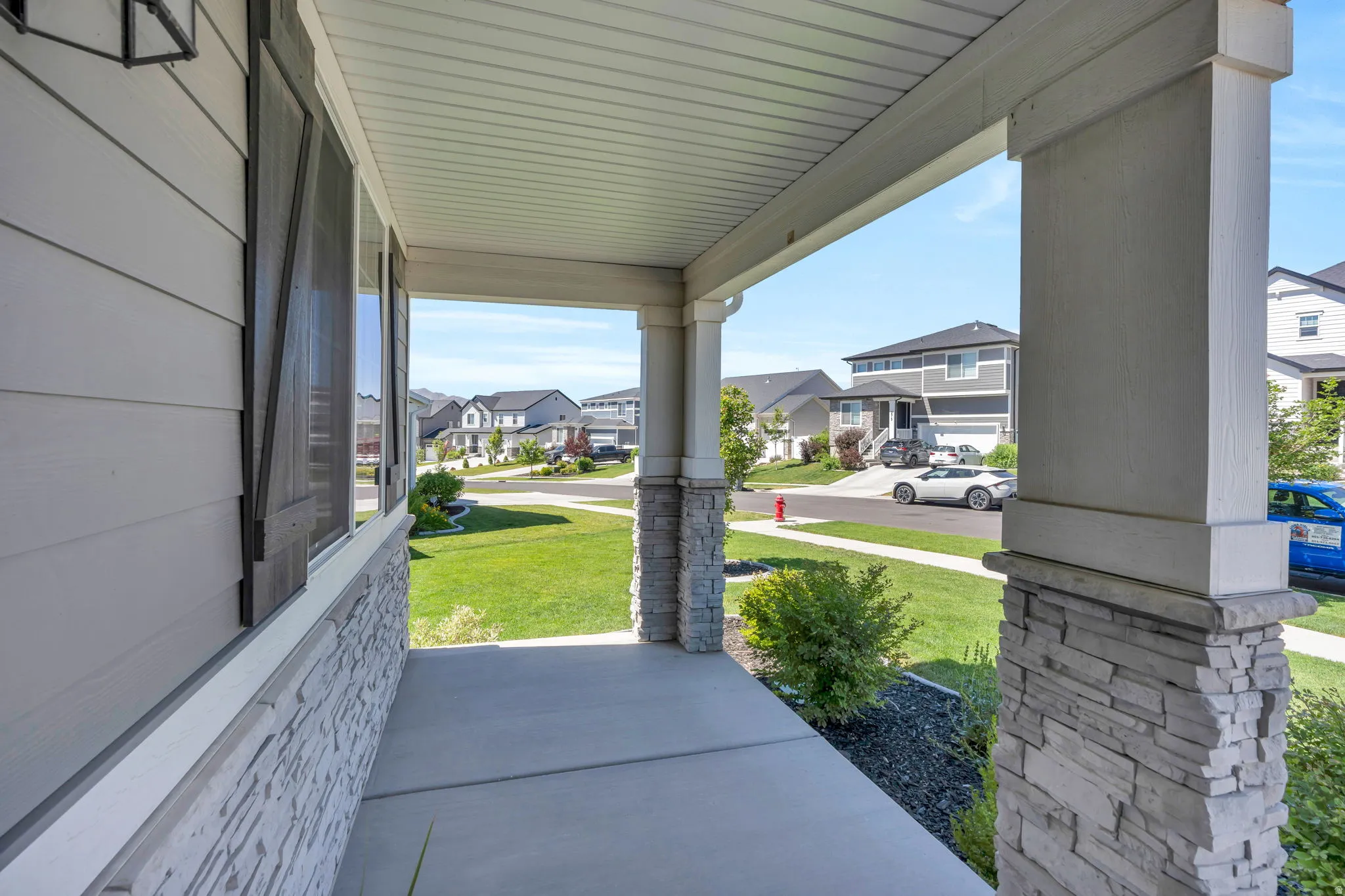Covered front porch featuring stacked stone column bases, siding exterior, and decorative window shutters