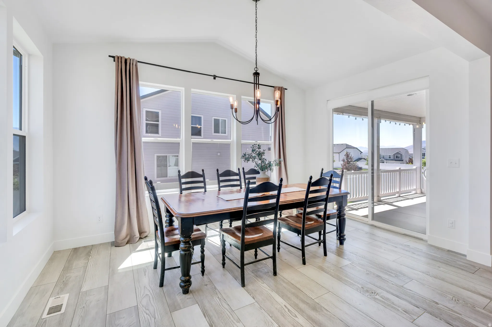 Dining space featuring wood-finish flooring, a vaulted ceiling, multiple windows, and sliding glass door access to an outdoor covered patio