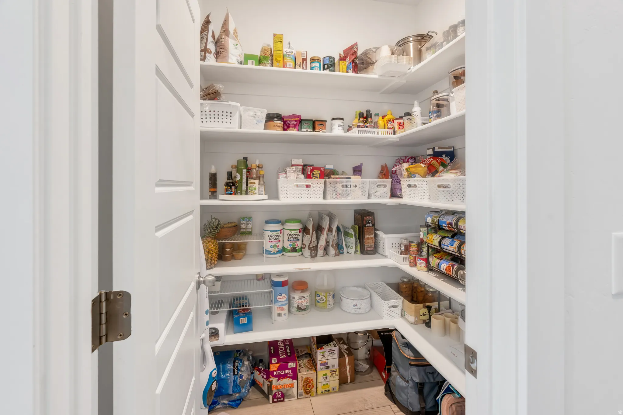 Spacious pantry featuring ample built-in shelving, white finish, and tiled flooring