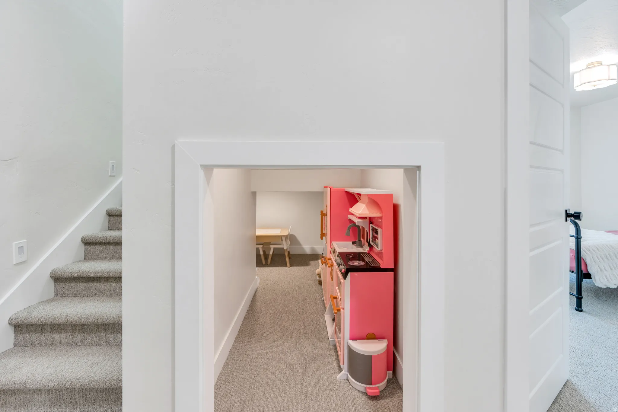 Carpeted staircase with white risers and handrail, featuring a separate arched doorway leading to a carpeted lower level space