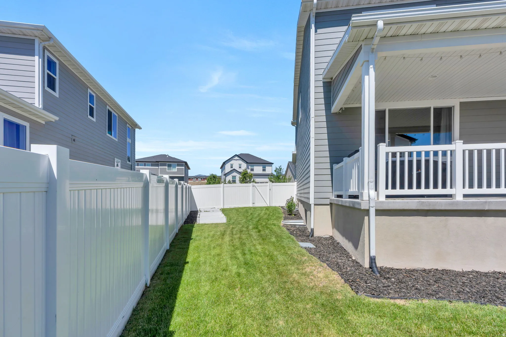 Expansive backyard featuring a manicured lawn, white vinyl fencing, and a covered patio with white railing