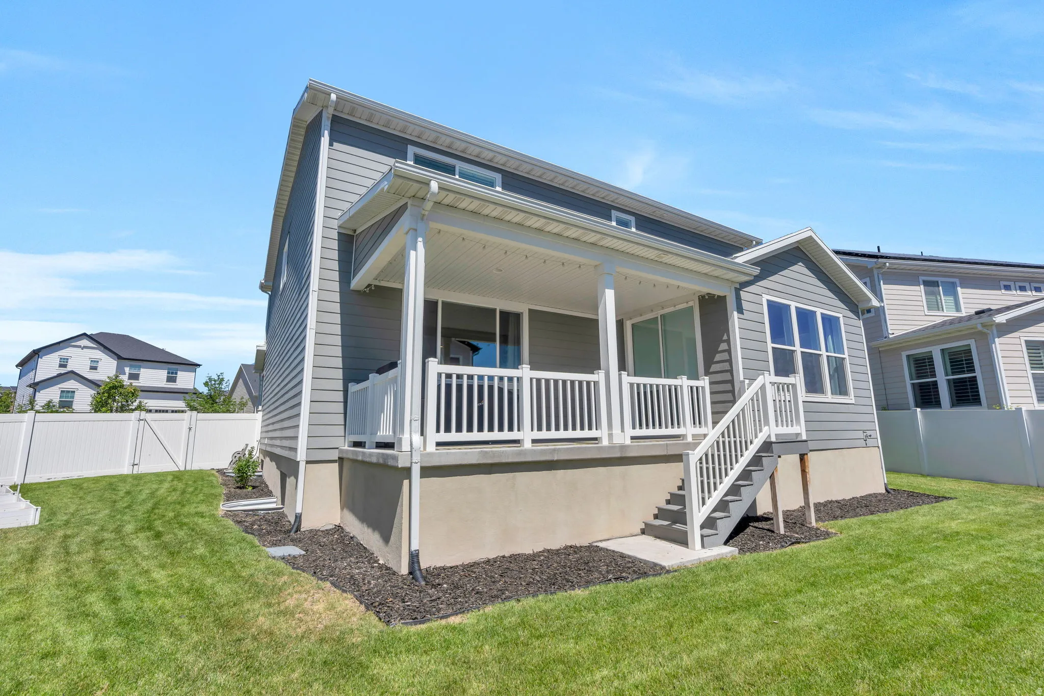 Rear exterior featuring a covered porch with white railings, gray siding, and a grass lawn