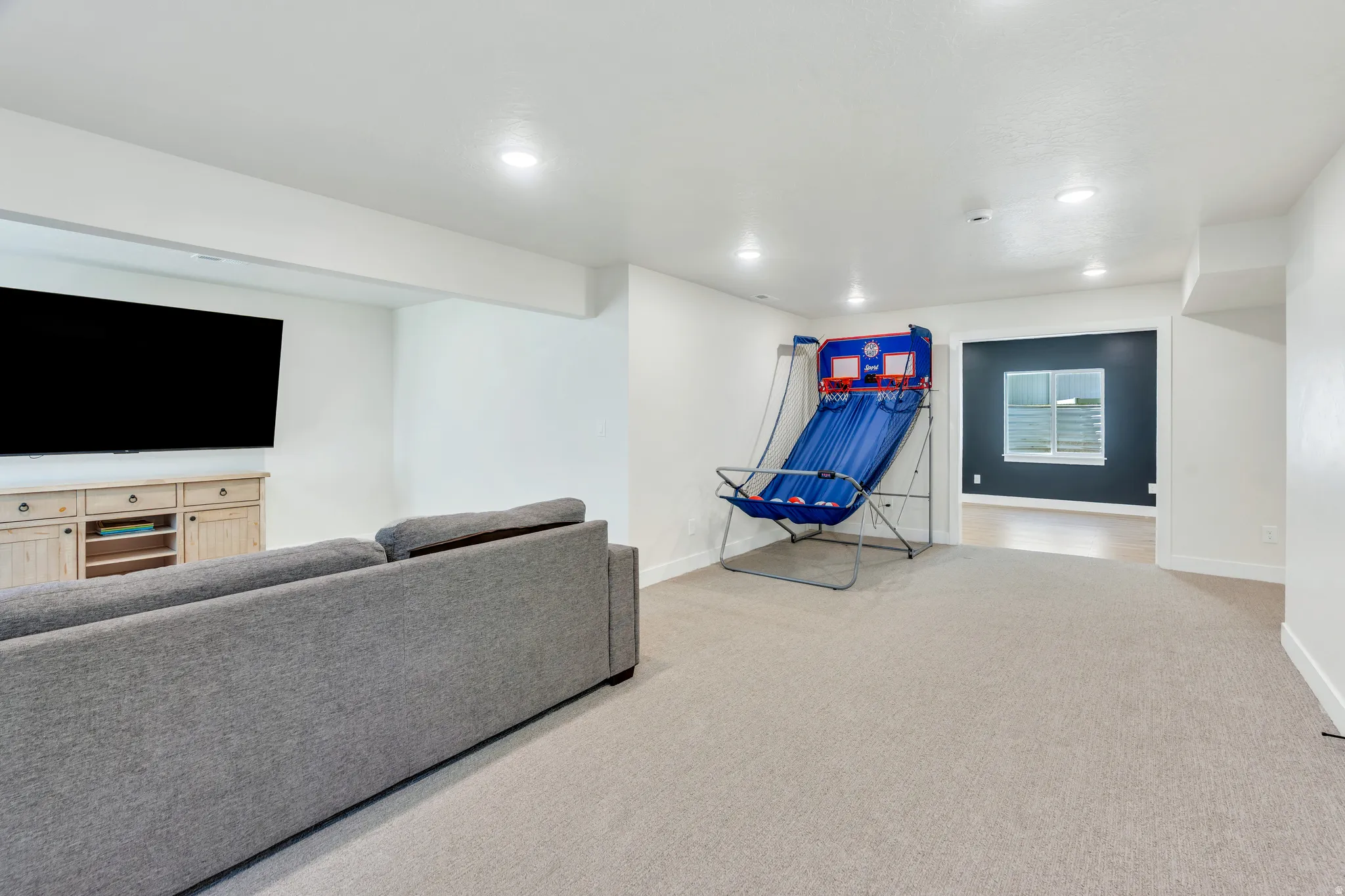 Spacious lower-level room featuring recessed lighting, light-colored carpeting, a wide framed doorway, and a window with horizontal blinds