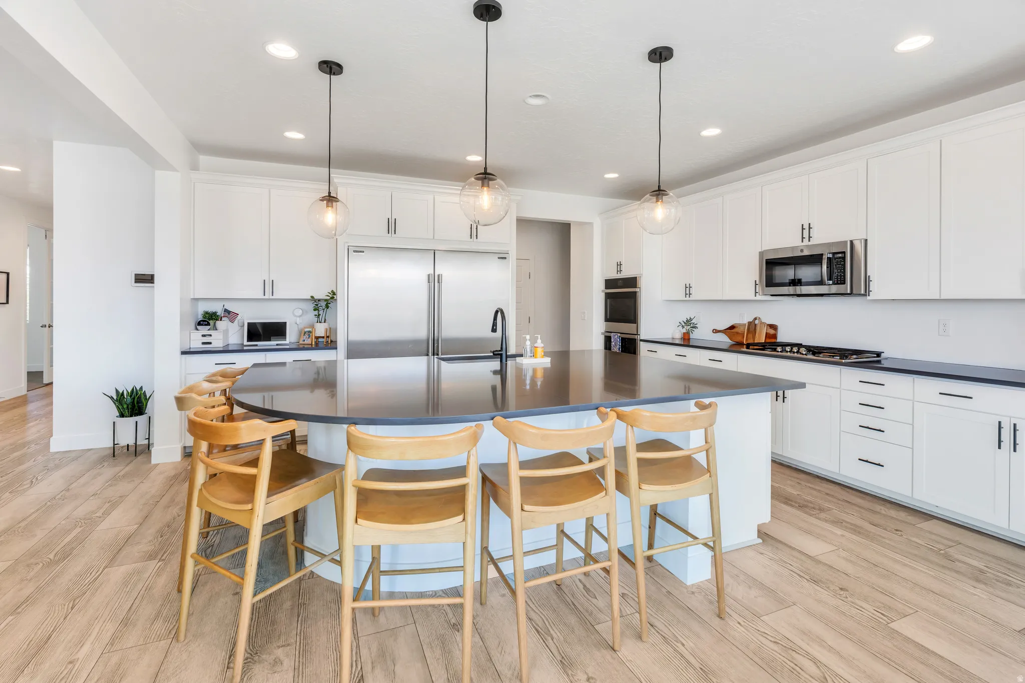 Spacious kitchen featuring an oversized island with dark countertops, white cabinetry with dark hardware, stainless steel appliances, and wood-finish flooring
