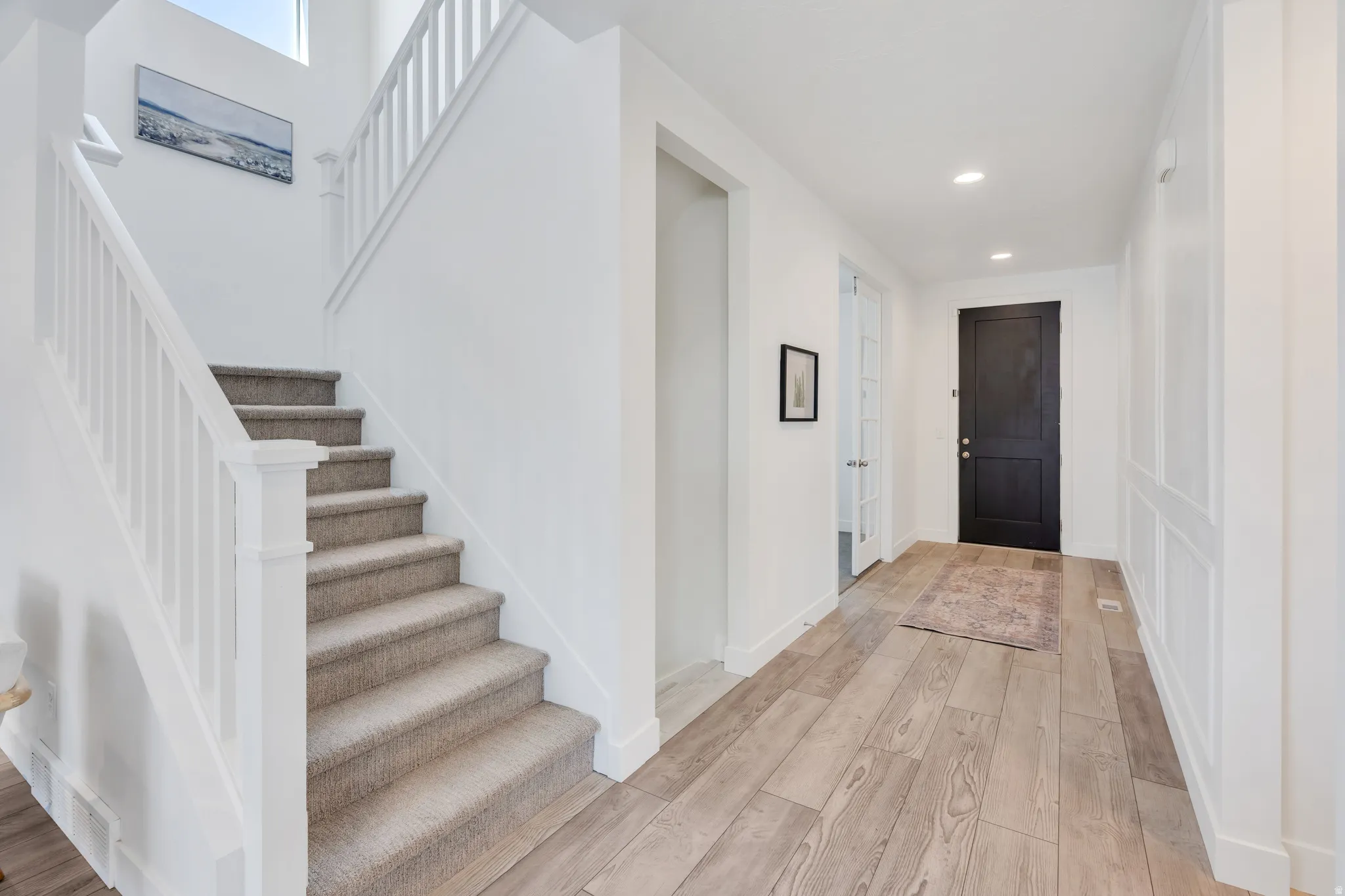 Entryway featuring light wood-finish flooring, white paneled walls, and a dark paneled door