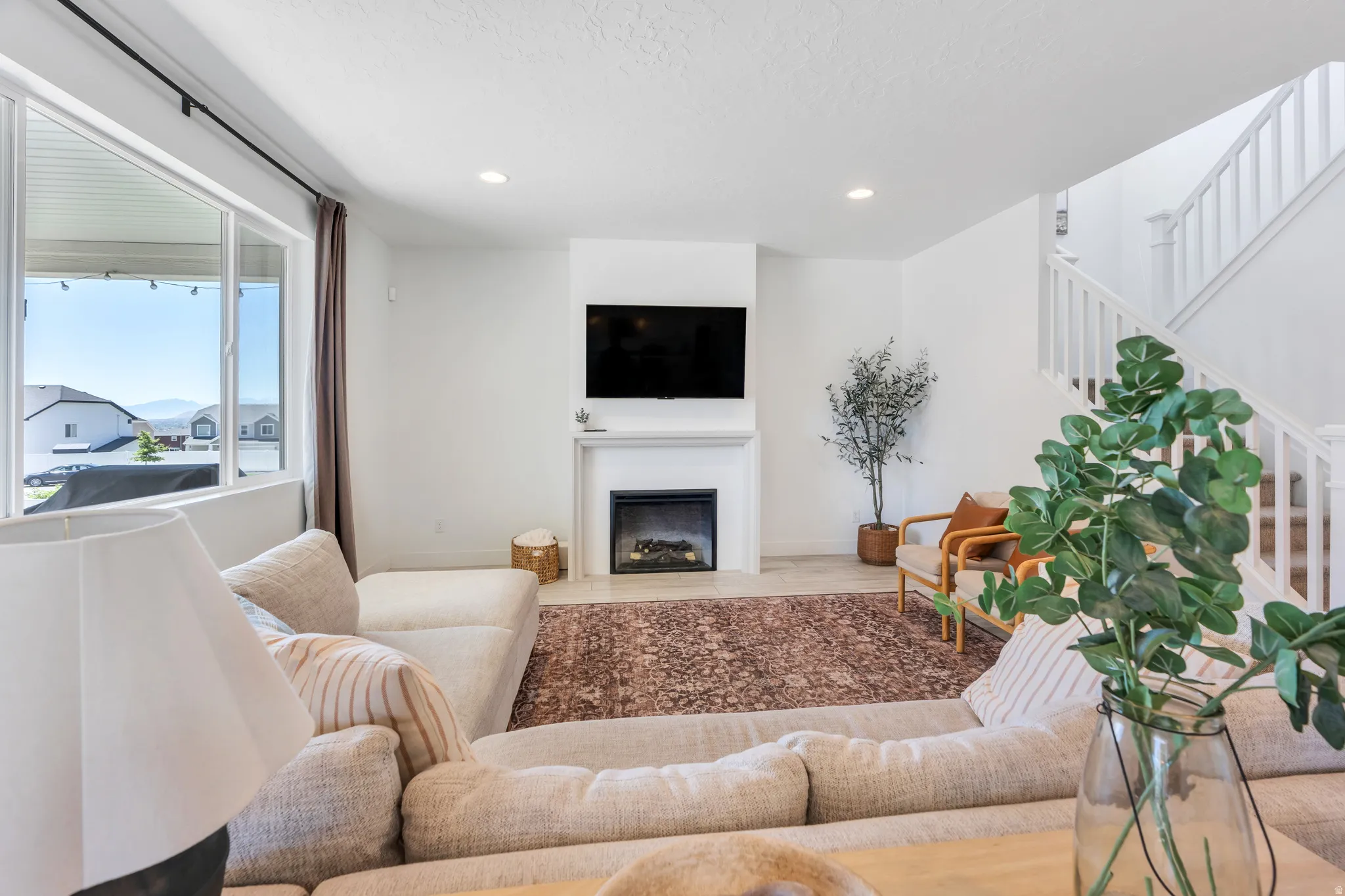 Living area featuring a fireplace with a white mantel, an expansive window, recessed lighting, and a staircase with white balusters
