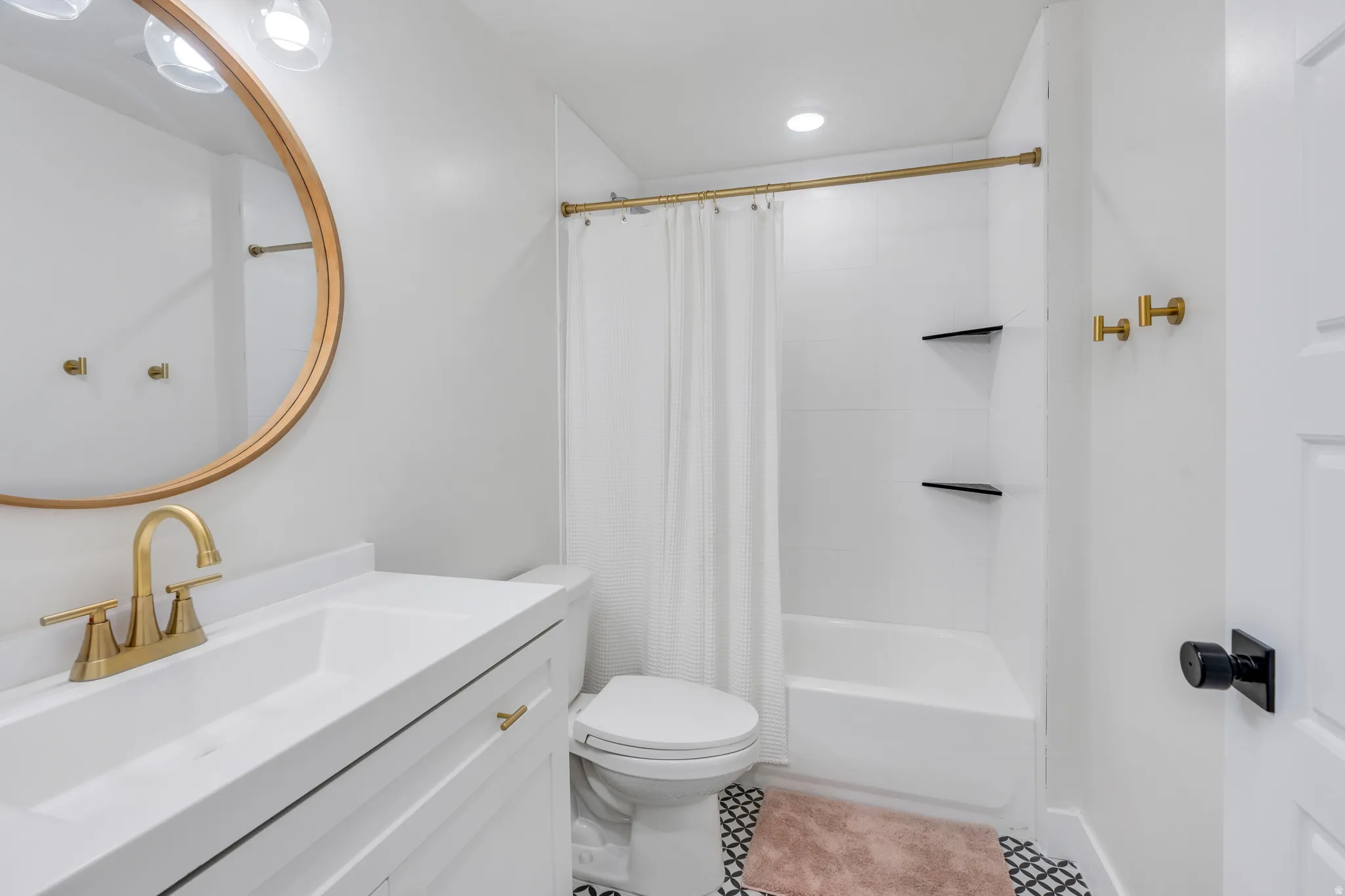 Bathroom featuring a white vanity with integrated sink, brass-finish faucet, and a round framed mirror