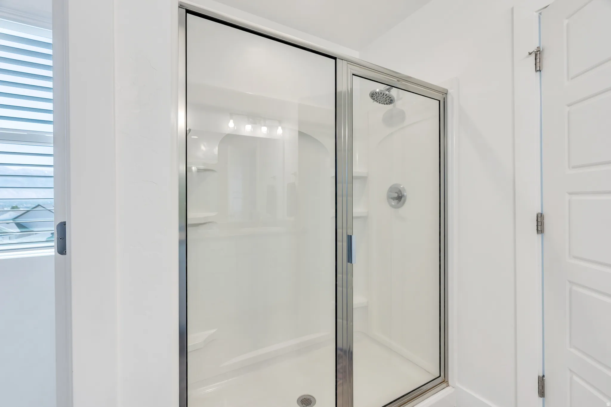Glass-enclosed shower featuring a built-in shower system, integrated shelving, and a bright white surround