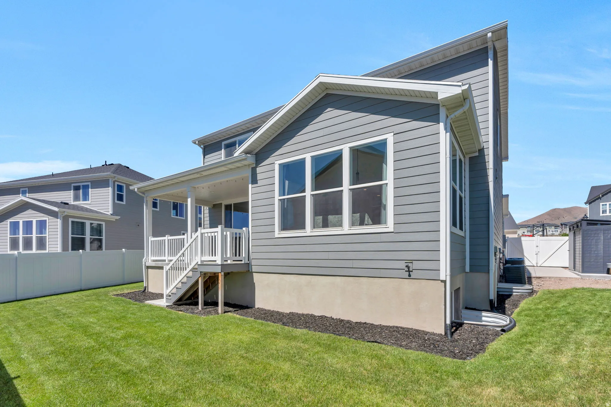 Rear exterior featuring gray siding, a covered patio with white railings, a concrete foundation, a manicured lawn, and a white privacy fence