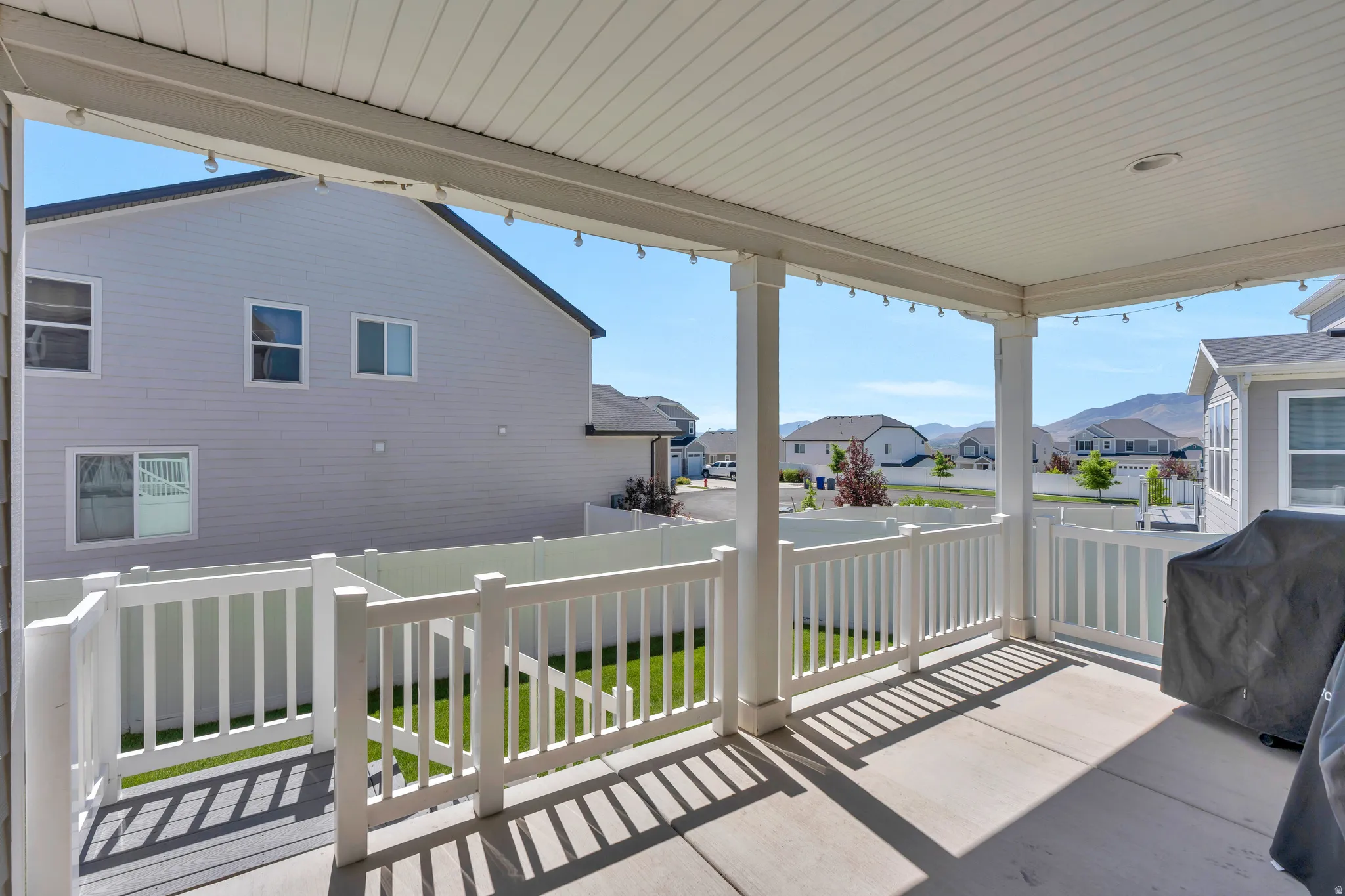 Covered patio with concrete flooring, white column supports, and a white picket railing