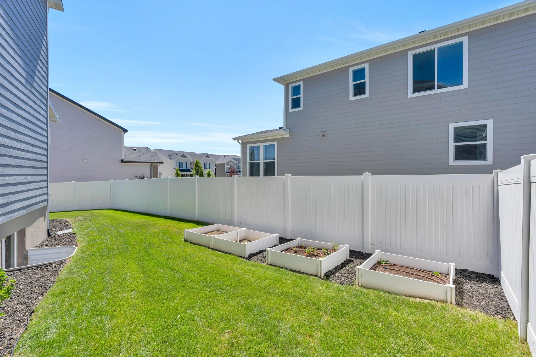 Expansive backyard featuring a manicured lawn, a white privacy fence, and three raised garden beds with irrigation