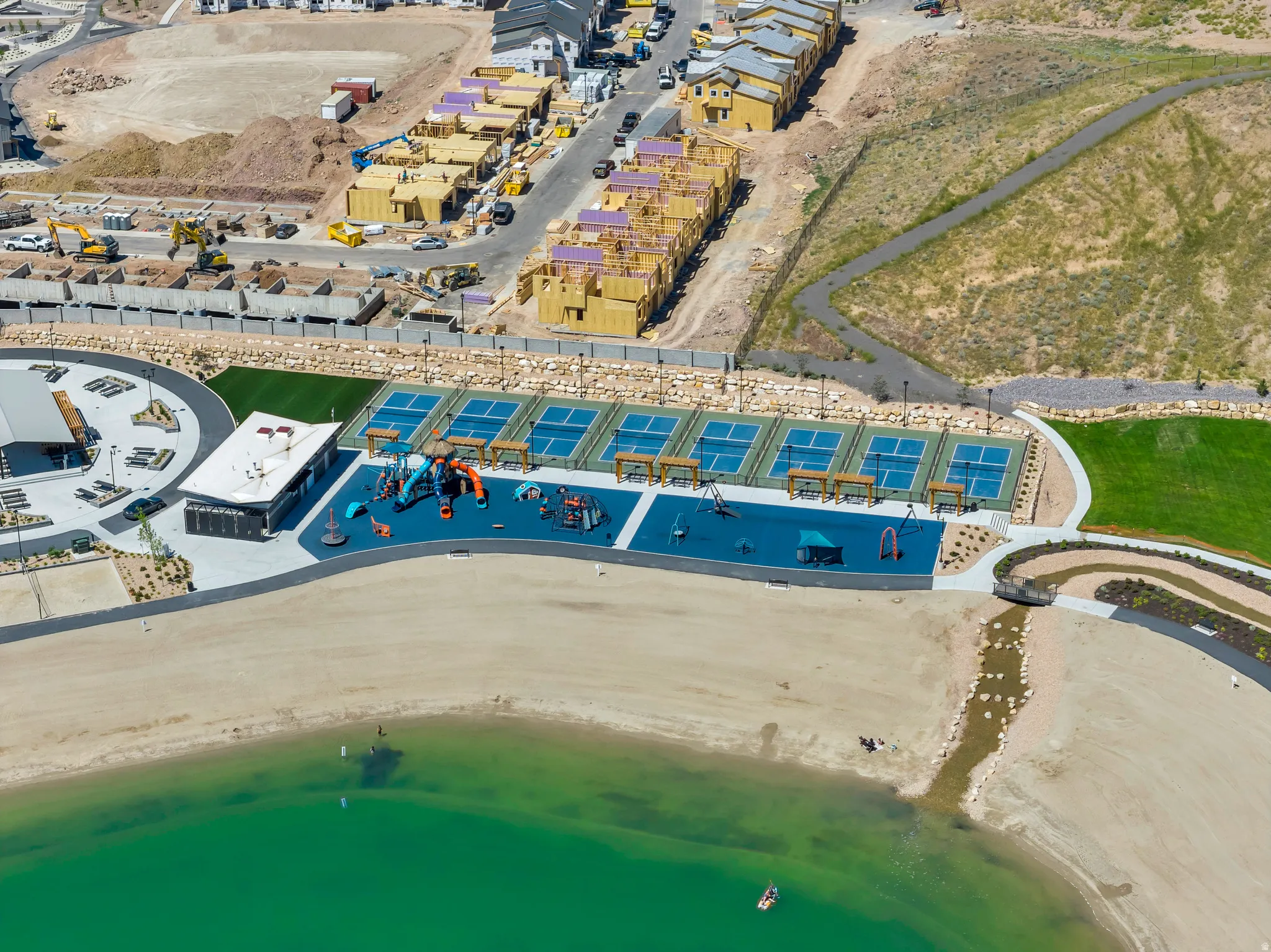 Expansive recreational area featuring multiple sports courts, a playground, and a sandy beach shoreline