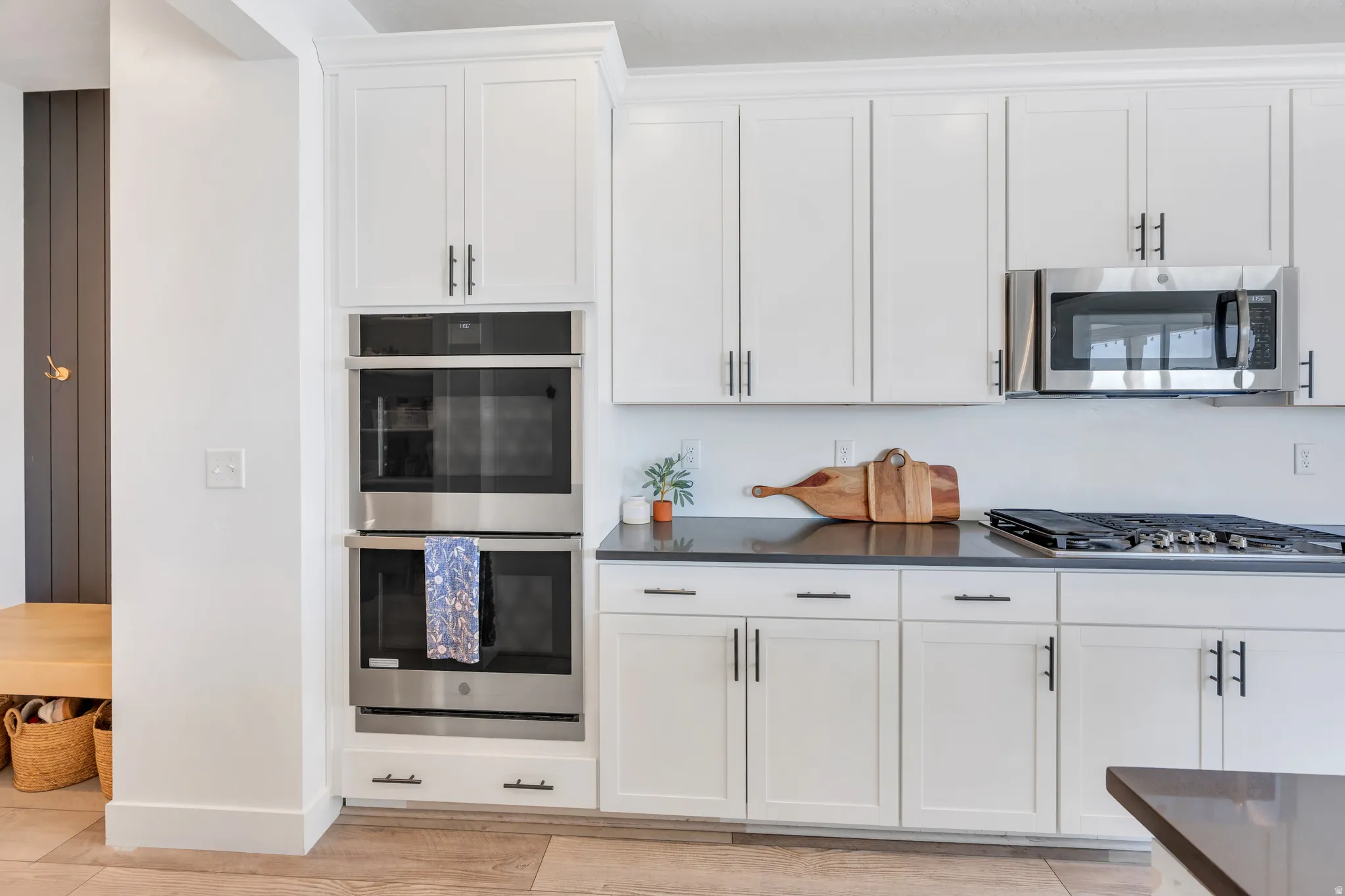 Modern kitchen featuring white shaker cabinetry, stainless steel appliances including double wall ovens and an over-range microwave, a gas cooktop, and dark countertops